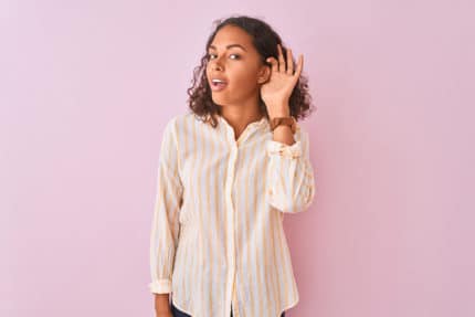 Une jeune femme brune en chemise tend l'oreille