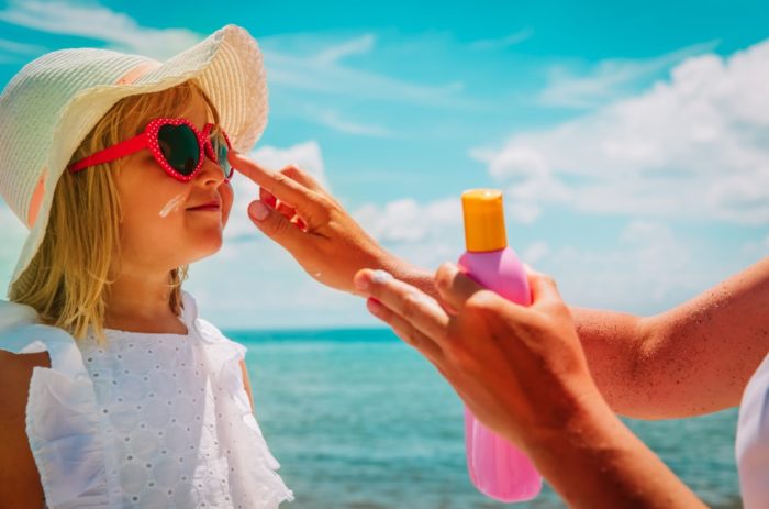 une mère met de la crème solaire sur le nez de sa fille protégée du soleil
