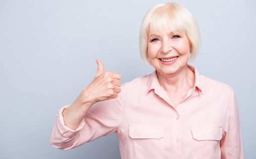 Old lady showing thumbs up gesture, smiling on grey background