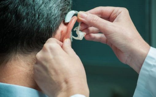 Doctor inserting hearing aid in senior's ear